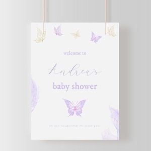 Puede incluir: Una invitación de baby shower blanca con mariposas moradas y amarillas. El texto dice "Bienvenido a la baby shower de Andrea. Estamos encantados de conocerte."
