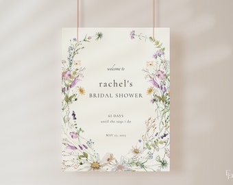 May include: A white bridal shower invitation with a floral wreath border. The text reads "welcome to rachel's bridal shower 61 days until she says i do may 27, 2023"
