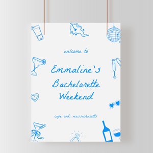 May include: A white sign with blue text and illustrations announcing "Welcome to Emmaline's Bachelorette Weekend, Cape Cod, Massachusetts". The illustrations include a cocktail glass, a heart, a bottle of wine, a ring, sunglasses, a disco ball, and a tube of lotion.