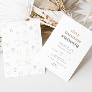 May include: A baby shower invitation with a light gray background and the text "tiny human shindig" in a colorful font. The invitation includes the date, time, and location of the event. The invitation also includes the names of the parents-to-be, Chelsea and Levi.