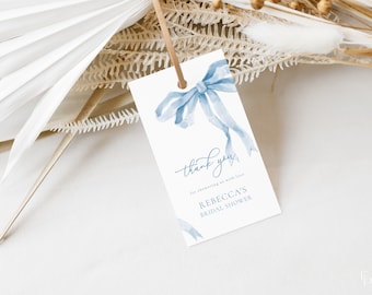 Può includere: Un fiocco blu ad acquerello con un'etichetta di ringraziamento che dice "Grazie per avermi riempito d'amore, la festa di addio al nubilato di Rebecca".