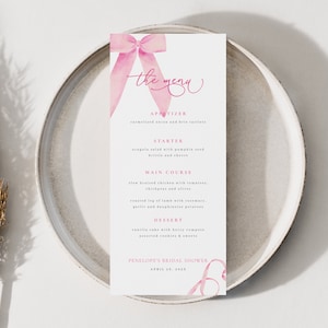 May include: A pink and white bridal shower menu with a pink ribbon bow at the top. The menu lists the appetizers, starter, main course, and dessert. The text at the bottom reads "Penelope's Bridal Shower, April 29, 2023."