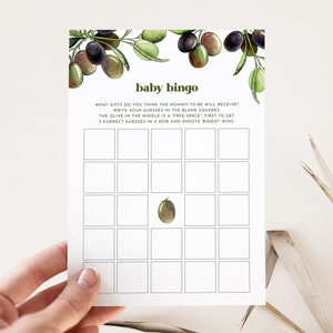 May include: A printable baby bingo card with a green olive in the center square. The card has a watercolor illustration of olive branches with green leaves and black olives at the top. The text on the card reads "baby bingo" and "WHAT GIFTS DO YOU THINK THE MOMMY TO BE WILL RECEIVE? WRITE YOUR GUESSES IN THE BLANK SQUARES. THE OLIVE IN THE MIDDLE IS A "FREE SPACE." FIRST TO GET 5 CORRECT GUESSES IN A ROW AND SHOUTS "BINGO" WINS."