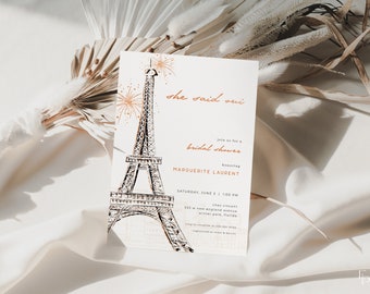 May include: A white bridal shower invitation with a hand-drawn illustration of the Eiffel Tower and fireworks. The text reads "she said oui" and "Join us for a bridal shower honoring Marguerite Laurent". The invitation includes the date, time, and location of the event.