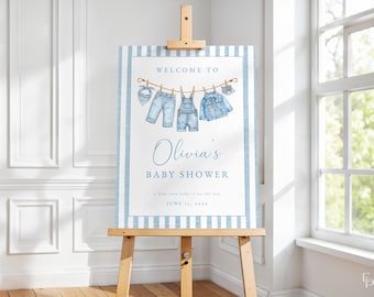 May include: A baby shower sign on a wooden easel. The sign has a blue and white striped border and features the words "Welcome to Olivia's Baby Shower." Watercolor illustrations of baby clothes hang on a clothesline. The date is June 24, 2023.