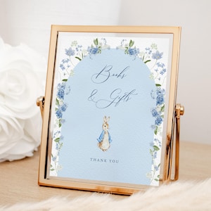 Peut inclure: Une pancarte bleue et blanche avec une bordure florale et une illustration de Lapin de Pâques. La pancarte indique "Livres & Cadeaux" et "Merci".