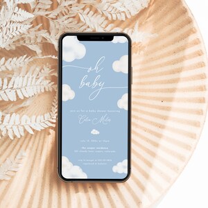 Pode incluir: Um convite para um ch&aacute; de beb&ecirc; azul e branco na tela de um smartphone. O convite apresenta um design de nuvens e o texto "oh baby" em uma fonte de escrita. O convite inclui a data, a hora e o local do ch&aacute; de beb&ecirc;.