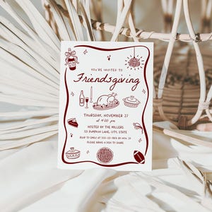 May include: A white invitation card with a burgundy border and illustrations for a Friendsgiving event. The text reads "You're invited to Friendsgiving" with details about the date, time, and location. The card includes illustrations of food and a football.