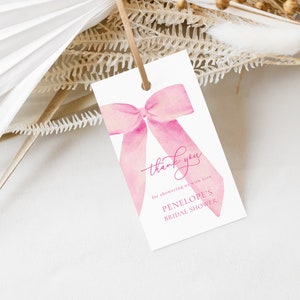 May include: A white gift tag with a pink watercolor bow and the words "thank you" in cursive. The tag also includes the text "for showering us with love. PENELOPE'S BRIDAL SHOWER."