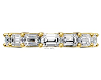 May include: A gold band ring featuring a series of rectangular, clear gemstones. The gemstones are set closely together, creating a continuous line of sparkle. The ring is set against a white background.