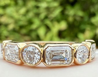 May include: A gold ring featuring an alternating pattern of bezel-set emerald-cut and round-cut clear stones. The band is crafted from polished yellow gold, showcasing a series of five prominent gemstones arranged horizontally across the top.