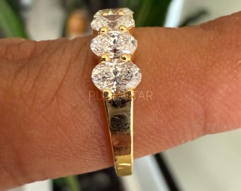 May include: A gold band ring with five clear oval-shaped gemstones.