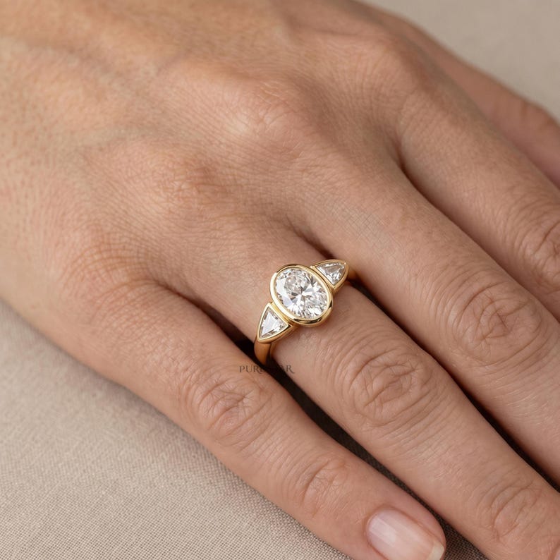 Three stone lab grown diamond bridal ring featuring oval center stone and bezel setting.