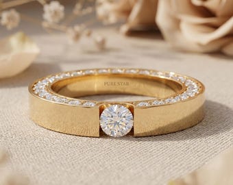 Puede incluir: Un anillo de banda de oro con un diamante central de talla brillante redonda, rodeado por una fila continua de diamantes más pequeños engastados en pavé a lo largo del borde superior. El interior del anillo tiene grabado PURE STAR.