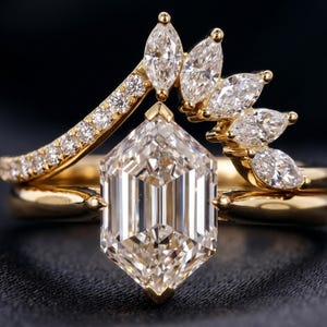 May include: A close-up of a gold engagement ring set with a large, hexagonal-cut diamond as the centerpiece. The ring is accompanied by a diamond-studded band and a separate band with marquise-cut diamonds. The setting is gold.