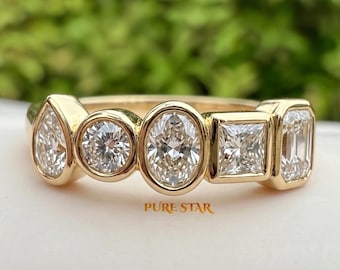May include: A gold ring featuring five bezel-set diamonds in various shapes, including pear, round, oval, princess, and emerald cuts, arranged horizontally. The text PURE STAR is printed in gold below the ring on the white surface.