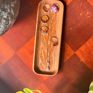 wooden catch all tray for jewellery  placed on a wooden table with green leaves and pots as photo features