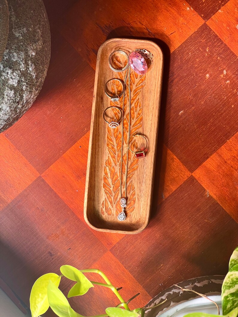 wooden catch all tray for jewellery  placed on a wooden table with green leaves and pots as photo features