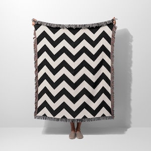 May include: Black and white woven throw blanket with a chevron pattern. The blanket has a fringe border.