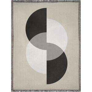 May include: A woven throw blanket with a geometric design featuring overlapping circles in black, white, and grey on a beige background.