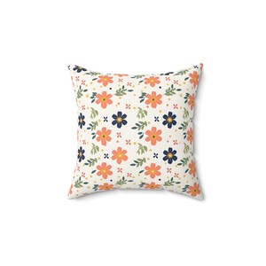 Könnte beinhalten: Ein weißes Kissen mit einem Blumenmuster. Das Muster zeigt kleine orangefarbene Blumen, blaue Blumen und grüne Blätter auf weißem Hintergrund.
