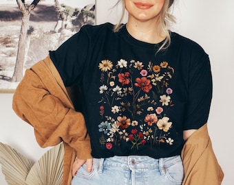 Może przedstawiać: Czarny T-shirt z nadrukiem kwiatowym przedstawiającym różne kwiaty w odcieniach czerwieni, różu, żółci i bieli.