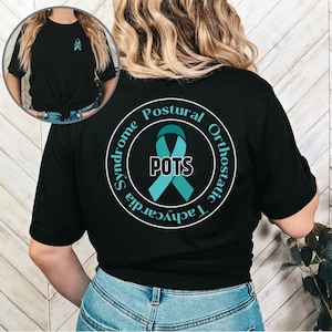 May include: Black t-shirt featuring a teal ribbon and the letters "POTS" within a circle, encircled by the words "Postural Orthostatic Tachycardia Syndrome". A smaller teal ribbon is also visible on the front.
