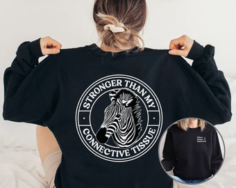 May include: Black sweatshirt with a white circle graphic on the back. The graphic features a zebra and the text "Stronger Than My Connective Tissue".