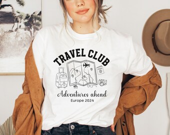 May include: White t-shirt with a black graphic design of a map, suitcase, camera, and glasses. The text "TRAVEL CLUB" is above the graphic and "Adventures ahead Europe 2024" is below the graphic.