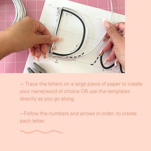 May include: A close-up of a person's hands bending a silver wire to form the letter "D" using a template with numbers and arrows. The template is on a white piece of paper with a pink background.