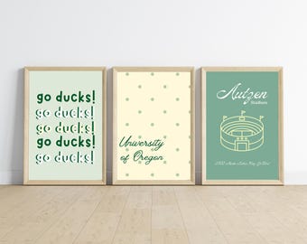 Könnte beinhalten: Drei gerahmte Kunstdrucke mit hellen Holzrahmen. Der linke Druck zeigt fünfmal wiederholt "go ducks!" in Grün. Der mittlere Druck hat die Worte "University of Oregon" in Grün. Der rechte Druck zeigt ein Stadion und sagt "Autzen Stadium".