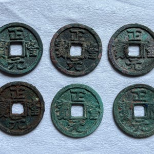 May include: Six antique Chinese coins with square holes in the center. The coins have a circular shape with visible inscriptions and a weathered, aged appearance, showing shades of green and brown.
