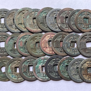 Könnte beinhalten: Eine Sammlung von einundzwanzig antiken chinesischen Münzen. Die Münzen sind rund mit quadratischen Löchern in der Mitte und bestehen aus einem bronzefarbenen Metall. Einige Münzen haben eine grüne Patina, und alle haben chinesische Schriftzeichen.