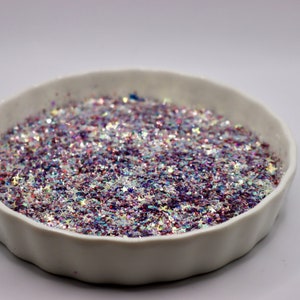 May include: A white bowl filled with iridescent glitter in shades of pink, purple, and white. The glitter is in the shape of stars.