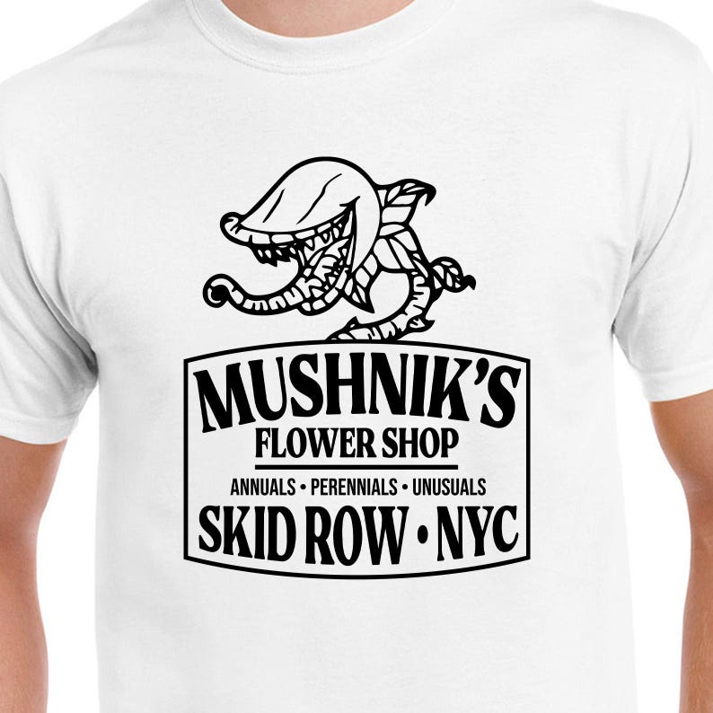Puede incluir: Camiseta blanca con una ilustraci&oacute;n en blanco y negro de una planta carn&iacute;vora y el texto "Mushnik's Flower Shop. Annuals - Perennials - Unusuasls. Skid Row. NYC."