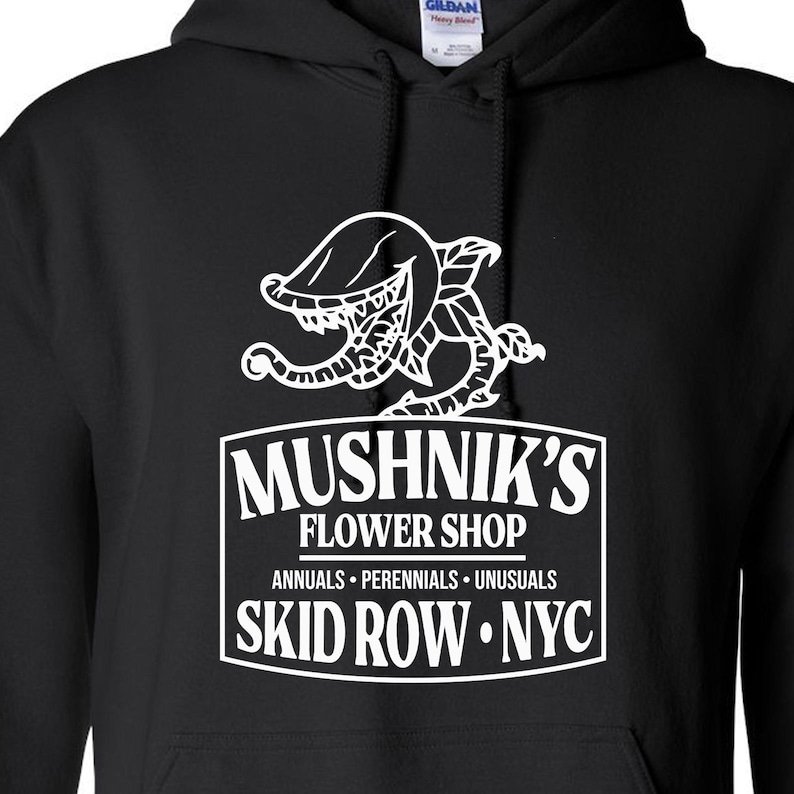 Puede incluir: Sudadera con capucha negra con un gr&aacute;fico blanco de una planta carn&iacute;vora y el texto "Mushnik's Flower Shop, Annuals - Perennials - Unusuasls, Skid Row - NYC."
