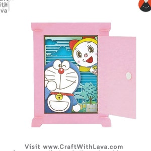 May include: A pink papercraft diorama with a pop-up scene featuring Doraemon and a character from the anime series, 'Chibi Maruko-chan'. The diorama is open to reveal the scene inside. The diorama is made by Craft With Lava.