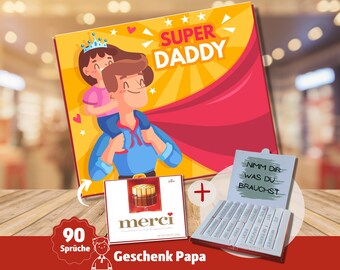 May include: A red and yellow gift box with a cartoon illustration of a father and daughter. The box says "Super Daddy" and includes a small box of chocolates and a box of 90 "Nimm dir was du brauchst" messages.