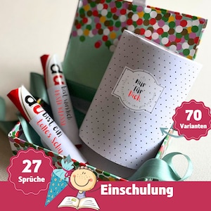 Op de afbeelding: Een cadeaudoos gevuld met kleurrijk confetti-patroonpapier en een witte doos met zwarte stippen. De witte doos heeft een sticker met de tekst "nur für dich", wat "alleen voor jou" betekent. De cadeaudoos bevat ook twee rood-witte snoeprepen met de tekst "du bist ein tolles Schy", wat "je bent een geweldig kind" betekent. De cadeaudoos is vastgebonden met een groen lint. De afbeelding bevat ook een rode cirkel met de tekst "70 Varianten", wat "70 variaties" betekent, en een rode cirkel met de tekst "27 Sprüche", wat "27 spreuken" betekent.