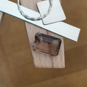 May include: A smoky quartz gemstone with a rectangular shape and a light brown colour.