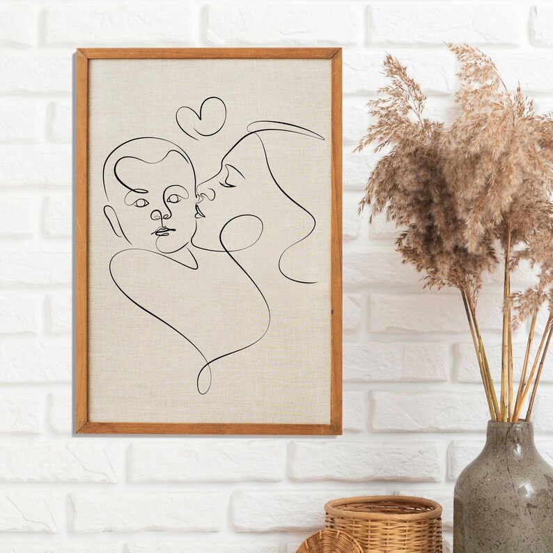 May include: A black and white line drawing of a mother and child embracing. The drawing is framed in a light brown wood frame and is hanging on a white brick wall.