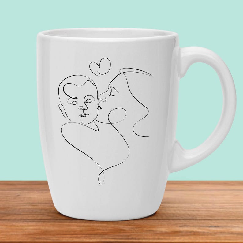 May include: White ceramic mug with a black line drawing of a mother and child. The mother is kissing the child on the cheek. A heart shape is drawn above their heads.