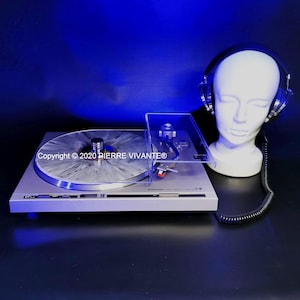 May include: A silver Pioneer turntable with a gray and white vinyl record. A clear plastic dust cover is open. A white mannequin head wears black headphones. The text "Copyright © 2020 PIERRE VIVANTE®" is visible.