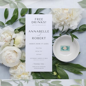 May include: A white card with the text "FREE DRINKS! AND THE WEDDING OF ANNABELLE and ROBERT HERE'S HOW IT GOES Music Plays We Say 'I Do' We Party! SATURDAY, MARCH 11, 20XX Melbourne, Australia - THANK YOU - Thank you for coming and sitting through this" on a blue background with white flowers.