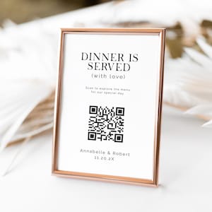 以下が含まれることがあります： 「DINNER IS SERVED (with love)」の黒い文字が書かれた、ローズゴールドのフレームに入った長方形のサイン。QRコードと「Annabelle & Robert」の名前と日付が含まれています。特別な日のために。