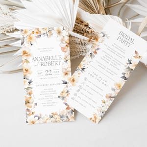 May include: Wedding ceremony program cards with a floral design in shades of beige, brown, and gray. The cards feature the names "Annabelle and Robert" and the date "Sat 22 Oct". One card lists the order of service, and the other card lists the bridal party and the plan for the day.