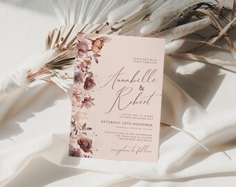 May include: A blush pink wedding invitation with floral accents. The invitation features the names "Annabelle & Robert" in elegant script, along with event details. The design includes a border of watercolor flowers in shades of burgundy, peach, and cream.