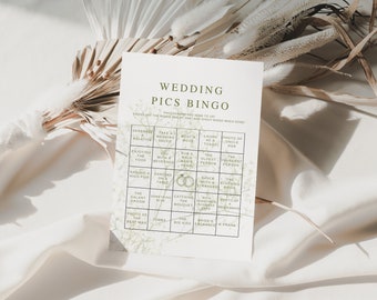 May include: A Wedding Pics Bingo card with a green floral design and the words "Wedding Pics Bingo" at the top. The card has a grid of squares with prompts like "Serenade a relative" and "Enjoying the food". The card is on a white surface.
