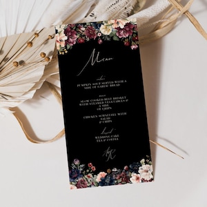 May include: Black wedding menu card with a floral border. The menu includes pumpkin soup, slow cooked beef brisket, chicken schnitzel, wedding cake, tea and coffee. The card is decorated with dark red, pink, and white flowers.