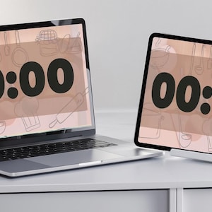 May include: A laptop and tablet display a timer set to 00:00. The screens have a light brown background with kitchen utensil illustrations. The laptop is open on a white surface, and the tablet is propped up on a stand.